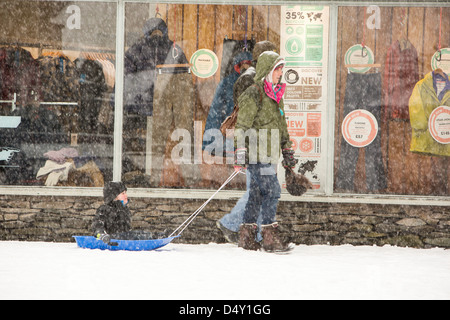 Un enfant d'être tiré sur un traîneau dans la neige à Ambleside, Lake District, UK. Banque D'Images