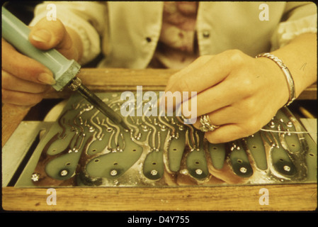 Cette photo montre un employé de la société 3M à New Ulm, Minnesota, travaillant avec un fer à souder sur un produit électronique. Il met en évidence la précision et la technologie impliquées dans le processus de fabrication de cette grande entreprise. Banque D'Images
