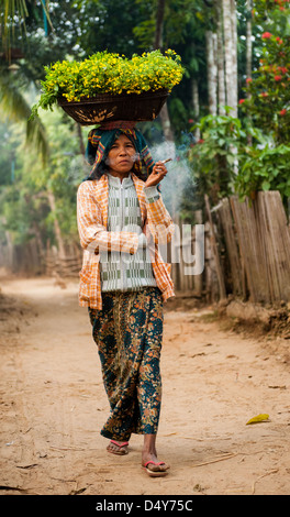 Femme avec panier de fleurs sur sa tête la marche dans son village le long de la rivière Chindwin Birmanie Myanmar Banque D'Images