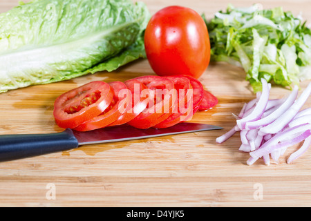 Photo horizontale de tranches de tomate, laitue, l'oignon avec un couteau sur une planche à découper en bambou naturel Banque D'Images