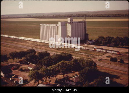 Le Southwest Limited (train no 3) est vu des airs alors qu'il passe devant un ascenseur coopératif agricole entre Dodge City et Garden City, au Kansas, en juin 1974. L'image met en évidence le lien entre le transport ferroviaire et les zones agricoles. Banque D'Images