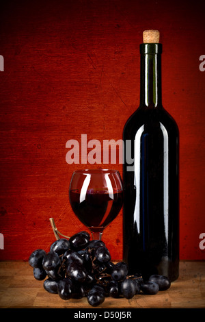 Bouteille de vin, le verre et les raisins sur rouge grunge background Banque D'Images
