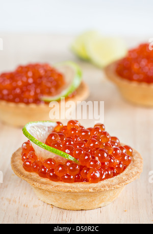 Tartelettes avec du caviar rouge et chaux sur fond de bois clair, selective focus Banque D'Images