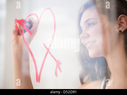 Hispanic girl drawing heart avec la flèche sur la fenêtre Banque D'Images