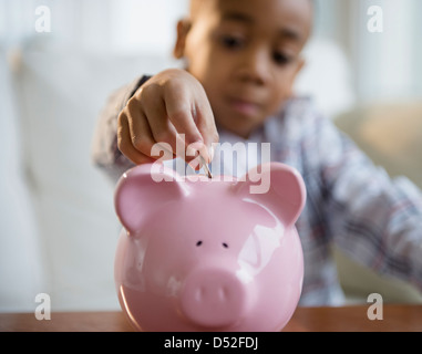 African American boy putting coins in piggy bank Banque D'Images