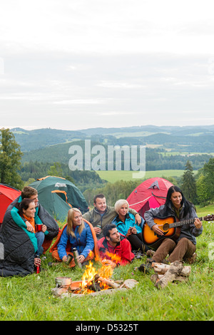 Groupe d'amis assis à côté des tentes, feu de camp girl playing guitar Banque D'Images