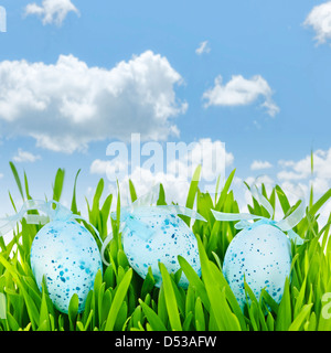 Trois oeufs de pâques mouchetée bleu avec des rubans dans l'herbe verte sur fond de ciel Banque D'Images