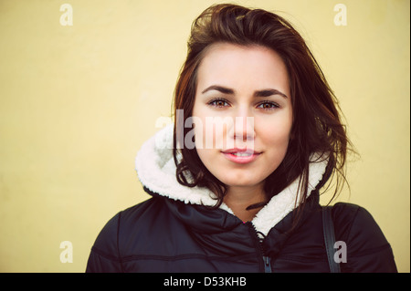 Femme brunette en modèle de mode veste noire en face de mur jaune Banque D'Images