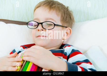 Peu fatigué garçon dans les verres dormir avec book in bed Banque D'Images
