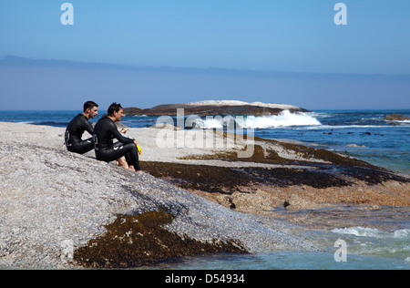 Deux nageurs en combinaisons s'asseoir sur Rock prendre du repos à la plage de Camps Bay - Cape Town, Afrique du Sud Banque D'Images