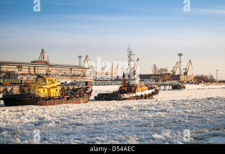 Petit bateau remorqueur va avec navire à travers le canal de glace dans le port de Saint-Pétersbourg port marchand Banque D'Images