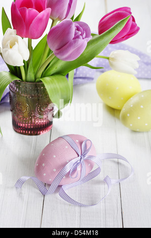 Rose, violet et blanc tulipes dans un vase en verre avec les oeufs de pâques sur fond de bois Banque D'Images