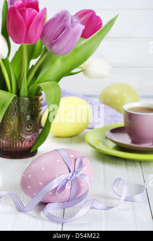 Rose, violet et blanc tulipes dans un vase en verre avec les oeufs de pâques sur fond de bois Banque D'Images