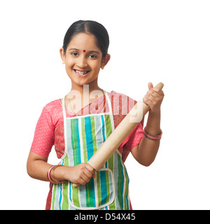 Portrait d'une fille imitant comme femme tenant un rouleau à pâtisserie et souriant Banque D'Images