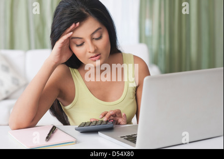 Femme assise en face d'un ordinateur portable à l'aide d'une calculatrice Banque D'Images