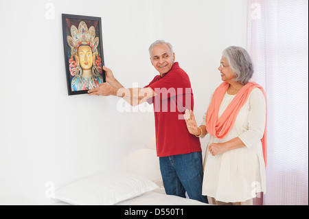 L'homme accroché un tableau sur un mur avec sa femme debout à côté de lui Banque D'Images