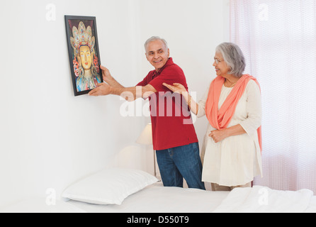 L'homme accroché un tableau sur un mur avec sa femme debout à côté de lui Banque D'Images