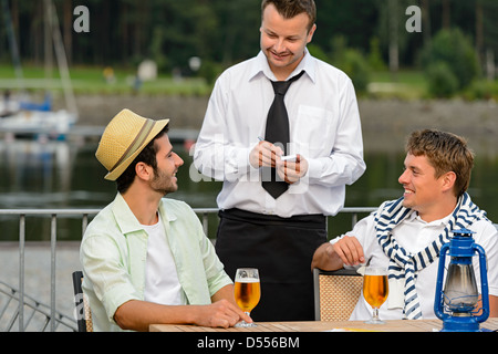 Smiling waiter taking order de clients hommes bar en plein air Banque D'Images