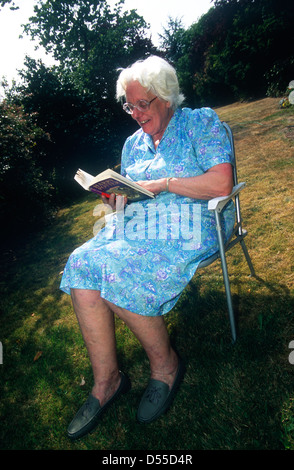 Femme âgée lecture Harry Potter et le Prisonnier d'Azbakan livre dans son jardin, Teddington, Middlesex, Royaume-Uni. Banque D'Images