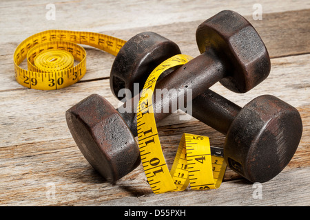 Une paire de vintage iron rusty haltères avec ruban jaune sur fond de bois grange peint en blanc - concept de remise en forme Banque D'Images