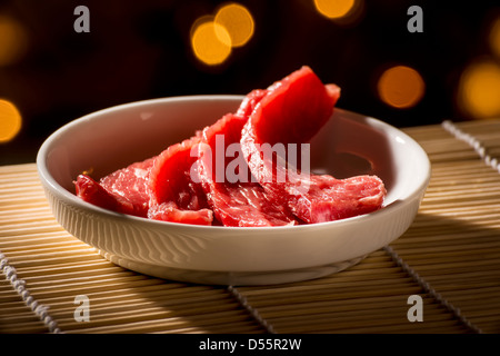 Sliced​​, rouge, de la viande crue dans un bol blanc sur un tapis de bambou Banque D'Images