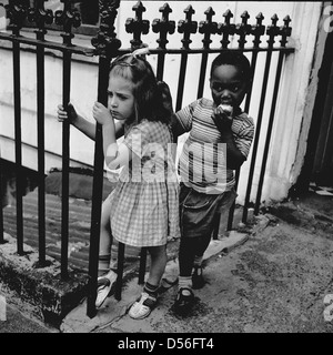 1950 historique. Inner London et deux enfants s'accrocher le fer forgé garde-corps de protection de l'époque victorienne en dehors d'une entrée privée. Banque D'Images