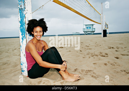 Mixed Race woman sitting by filet de volley-ball sur plage Banque D'Images
