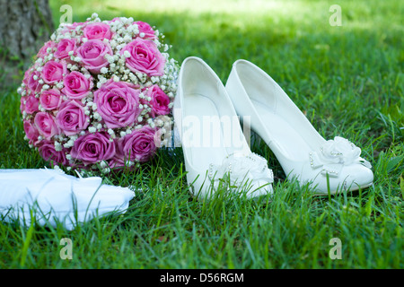 Chaussures blanc bouquet rose, de roses et d'un beau sac à main de la mariée sur une herbe verte Banque D'Images