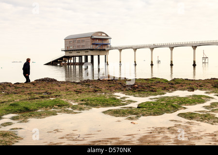 Un homme qui marche sur la plage, l'observation de la station de sauvetage de la RNLI à Bembridge sur l'île de Wight prises de Lane End Beach Banque D'Images