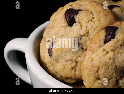 Une photographie du gros soft, des cookies aux pépites de chocolat dans une tasse à café blanche sur fond noir. Banque D'Images