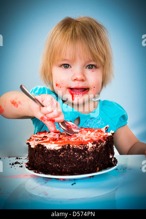 Petite fille manger un gâteau sur un fond bleu Banque D'Images