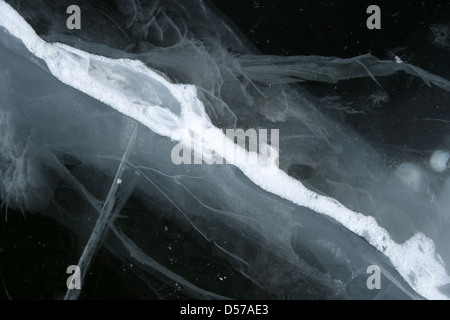 Résumé fond glace neige fissurée. L'eau d'un noir profond d'une rivière gelée. Banque D'Images
