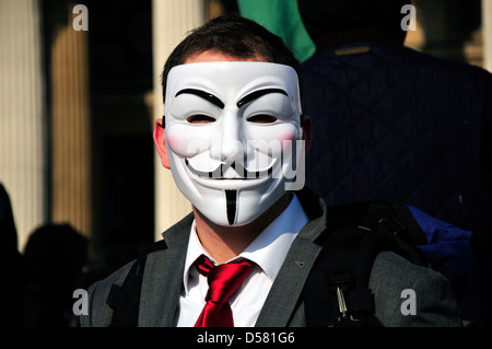 Un homme avec une cravate rouge portant un masque anonyme lors d'un rassemblement à Trafalgar Square, Londres, UK Banque D'Images