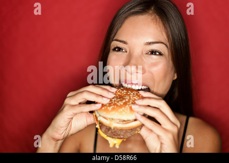 Happy mixed race caucasienne / Asian woman en mangeant burger isolé sur fond rouge Banque D'Images