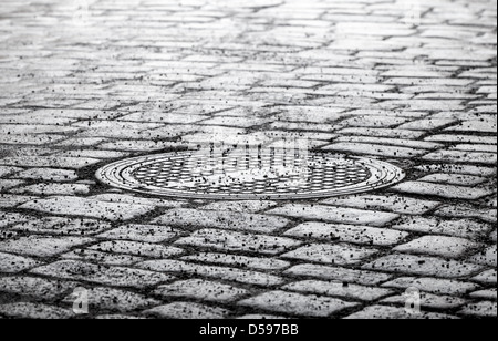 Acier ronde d'égout sur dark old cobblestone road Banque D'Images