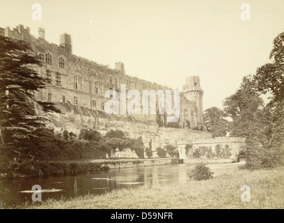 Une vue du château de Warwick à Warwick, en Angleterre, avec ses murs de fortification, ses parapets et ses douves. Le château, un exemple important de l'architecture médiévale, est entouré de plans d'eau et de plantes luxuriantes, avec des créneaux et des tours visibles dans toute la structure. Banque D'Images