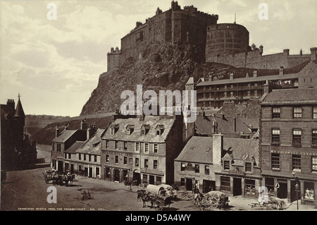 Cette photographie montre le château d'Édimbourg vu du quartier de Grassmarket, offrant un aperçu des fortifications du château et de la scène urbaine animée qui l'entoure, y compris les chevaux et les activités du marché. Banque D'Images