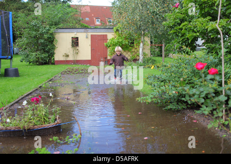 Handewitt, Allemagne, un garçon s'exécute en bottes de caoutchouc à travers un jardin inondé Banque D'Images