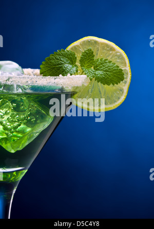 Gros plan du cocktail vert dans un verre à martini avec bord sucrées, lime slice, cubes de glace, feuille de menthe