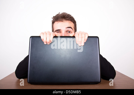 Jeune homme assis derrière un ordinateur portable avec un clin d'un oeil et de préhension difficile sur l'écran Banque D'Images