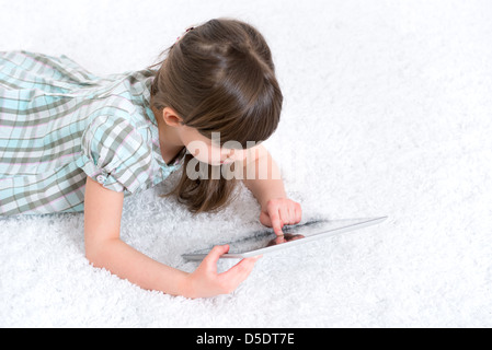 Jeune fille (6-7 ans) à la recherche et à jouer avec une tablette numérique en salle blanche. Banque D'Images