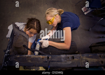 Le port de lunettes de sécurité deux adolescentes travailler ensemble sur une voiture en auto shop class à San Clemente, CA. Banque D'Images