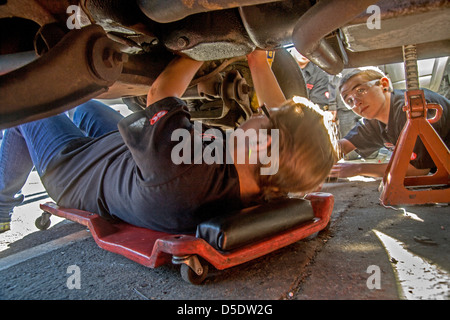 Le port de lunettes de sécurité un Caucasian teenage girl and boy travailler sous un moteur de voiture en auto shop class à San Clemente, CA. Banque D'Images