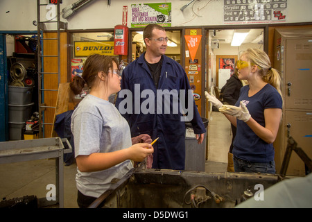 Le port de lunettes de sécurité deux adolescentes de parler avec leur professeur avec qui ils travaillent dans une voiture à auto shop class Banque D'Images