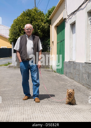 Homme âgé marcher un chien et à la recherche à l'appareil photo dans un milieu urbain et sur une journée ensoleillée Banque D'Images