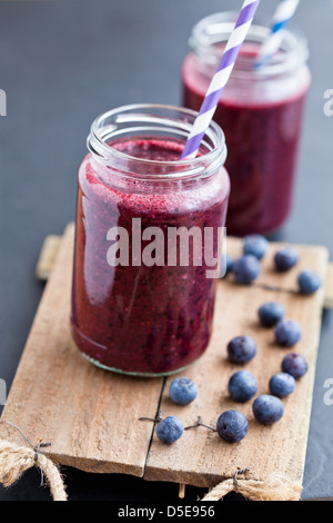 Libre de blueberry smoothies en verres avec des pailles à rayures sur le plateau de service en bois avec des bleuets Banque D'Images