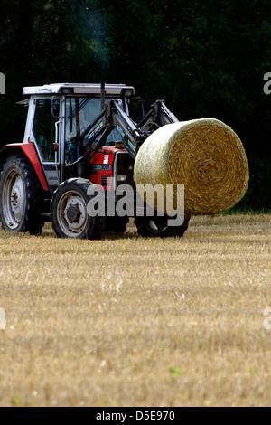 Agriculteur du levage d'une botte de paille avec tracteur, UK Banque D'Images