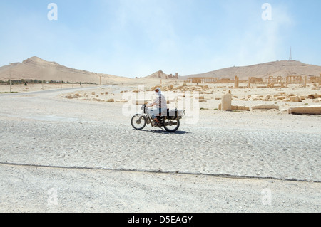 Motorcyclist riding en bas de la route sur l'arrière-plan de la ville antique de Palmyre, Syrie Banque D'Images