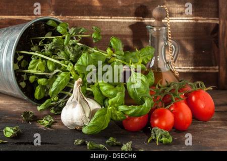 Dans la benne de basilic frais, de l'ail et les tomates cerises rouges sur table en bois avec l'huile d'olive dans une bouteille en verre vintage Banque D'Images