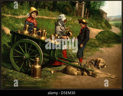 Une scène à Bruxelles, en Belgique, avec des vendeurs de lait. L'image montre un garçon avec un chariot en laiton, vêtu d'un costume, tout en versant du lait, mettant en valeur le commerce quotidien au début du XXe siècle à Bruxelles. Banque D'Images